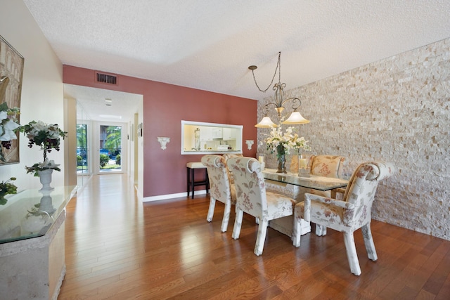 dining room featuring wood-type flooring, a textured ceiling, and an inviting chandelier