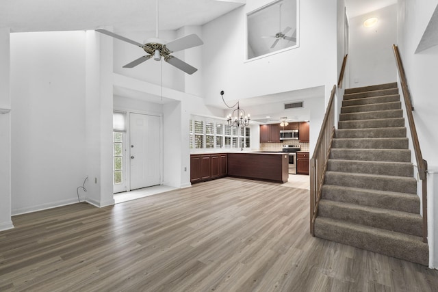 unfurnished living room with hardwood / wood-style floors, a towering ceiling, and ceiling fan with notable chandelier