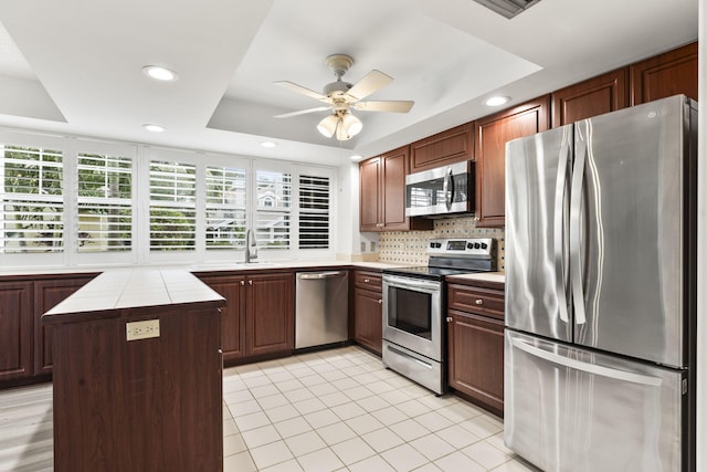 kitchen featuring stainless steel appliances, a tray ceiling, ceiling fan, a center island, and tile counters