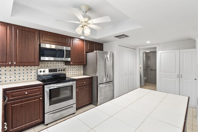 kitchen with ceiling fan, tasteful backsplash, tile countertops, a tray ceiling, and appliances with stainless steel finishes