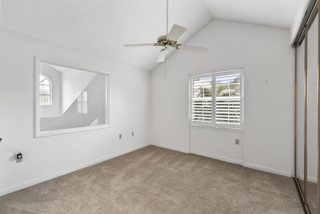 spare room with a textured ceiling, light colored carpet, vaulted ceiling, and ceiling fan