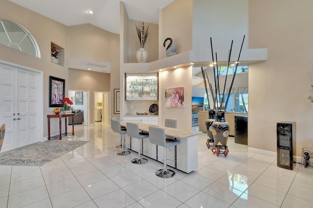 kitchen with a breakfast bar, white cabinetry, light tile patterned floors, and a high ceiling