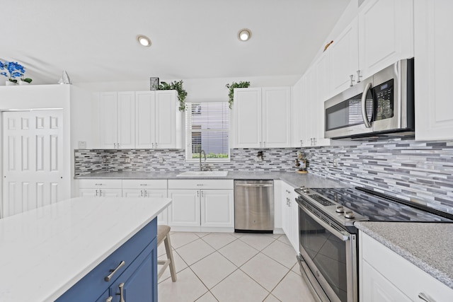 kitchen with appliances with stainless steel finishes, sink, white cabinets, light tile patterned floors, and blue cabinets