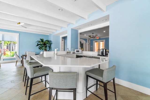 kitchen featuring kitchen peninsula, a breakfast bar, ceiling fan, sink, and beamed ceiling