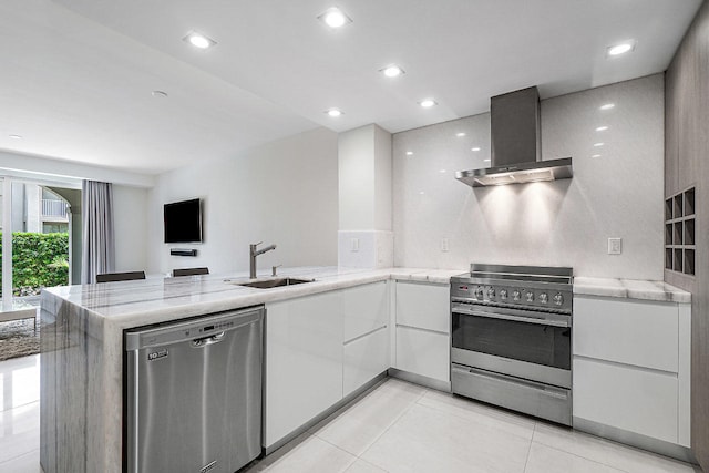 kitchen with wall chimney range hood, sink, white cabinetry, kitchen peninsula, and stainless steel appliances