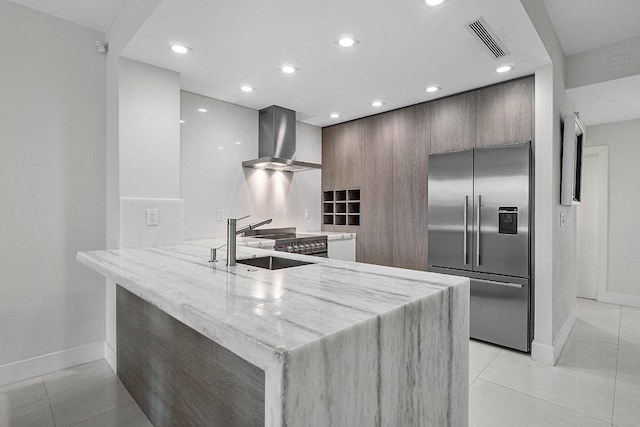 kitchen with stainless steel refrigerator with ice dispenser, wall chimney exhaust hood, light tile patterned floors, light stone counters, and kitchen peninsula