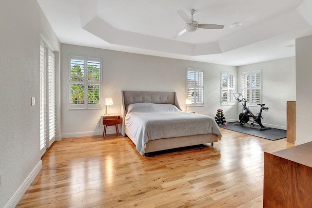 bedroom with a tray ceiling, ceiling fan, and light wood-type flooring