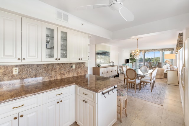 kitchen featuring ceiling fan with notable chandelier, white cabinetry, dark stone countertops, and backsplash