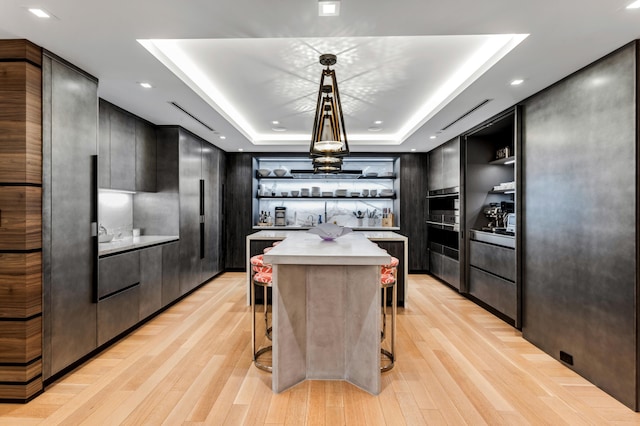 kitchen with a tray ceiling, a breakfast bar area, decorative light fixtures, and light wood-type flooring