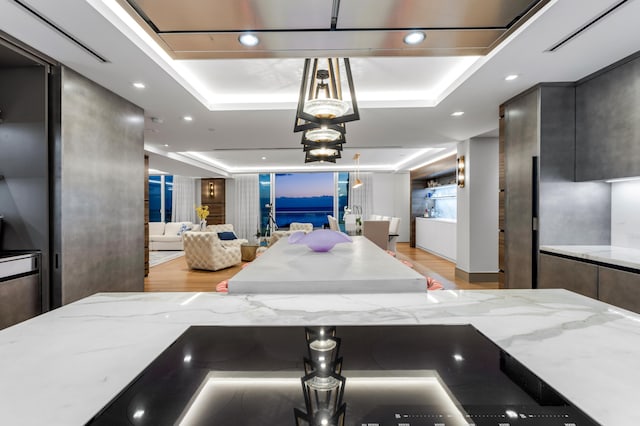 kitchen with light wood-type flooring, decorative light fixtures, a raised ceiling, and light stone counters