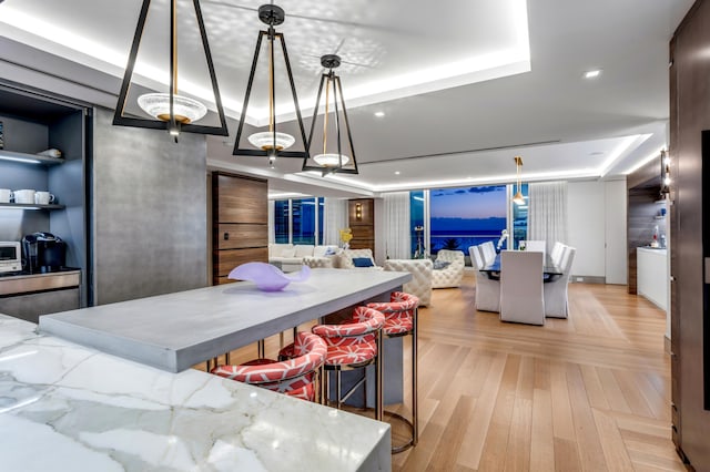 kitchen with pendant lighting, light wood-type flooring, a raised ceiling, and light stone counters