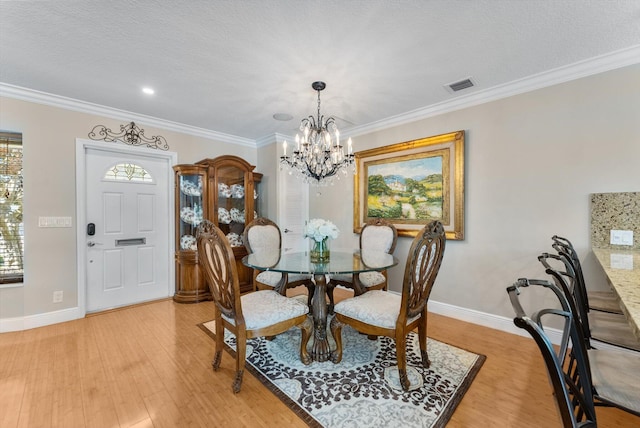 dining room featuring crown molding, light hardwood / wood-style flooring, a textured ceiling, and an inviting chandelier