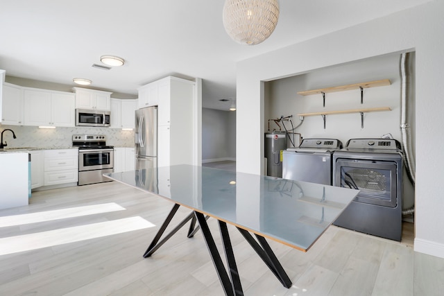 kitchen with backsplash, electric water heater, stainless steel appliances, washer and dryer, and white cabinetry