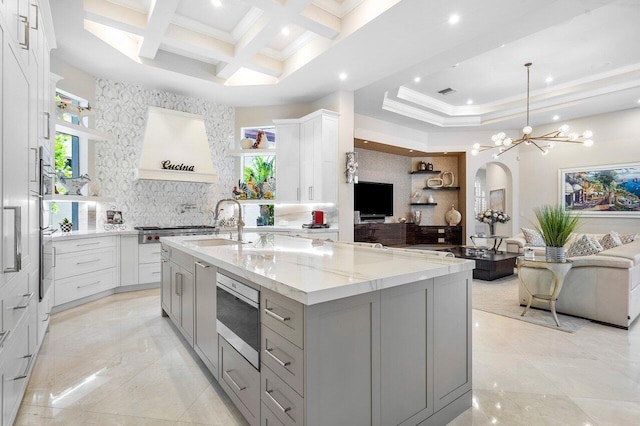 kitchen with pendant lighting, coffered ceiling, a spacious island, beam ceiling, and light stone counters