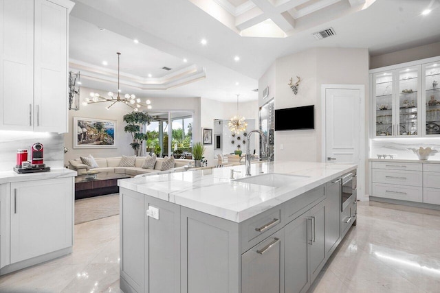 kitchen with light stone countertops, gray cabinets, a spacious island, and sink