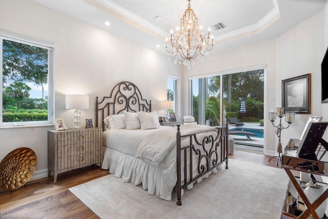 bedroom with a tray ceiling, multiple windows, a chandelier, and hardwood / wood-style flooring