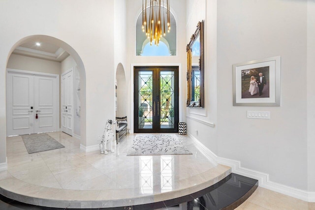 foyer featuring french doors, a towering ceiling, a chandelier, and ornamental molding