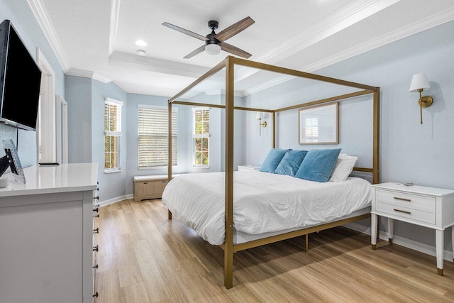 bedroom with ceiling fan, a tray ceiling, ornamental molding, and light hardwood / wood-style flooring