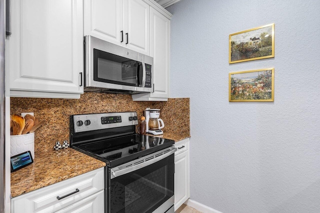 kitchen featuring stainless steel appliances, white cabinetry, and dark stone counters