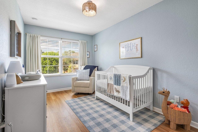 bedroom featuring a textured ceiling, light wood-type flooring, and a crib