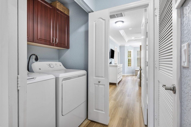 laundry area with washing machine and dryer, light wood-type flooring, ornamental molding, a textured ceiling, and cabinets