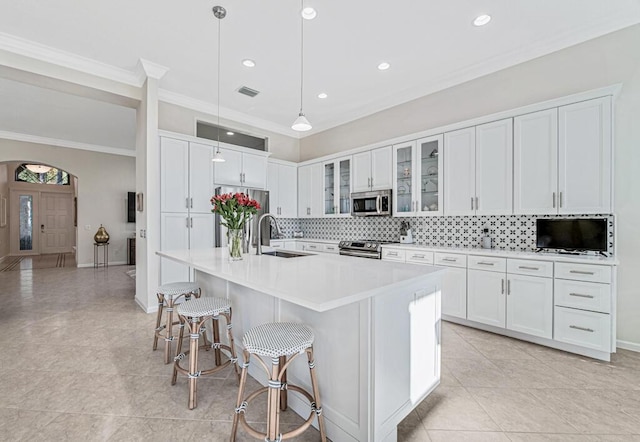 kitchen featuring stainless steel appliances, a kitchen island with sink, sink, decorative light fixtures, and white cabinets