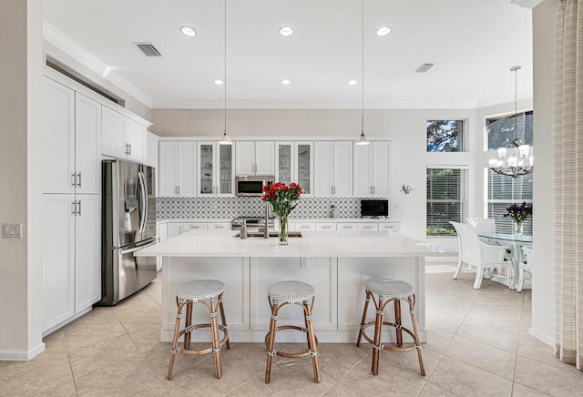 kitchen featuring pendant lighting, a kitchen island with sink, white cabinets, appliances with stainless steel finishes, and a kitchen bar