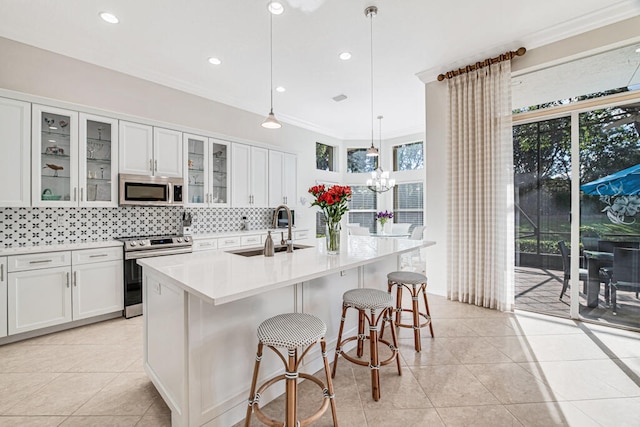 kitchen with white cabinets, hanging light fixtures, an island with sink, and stainless steel appliances