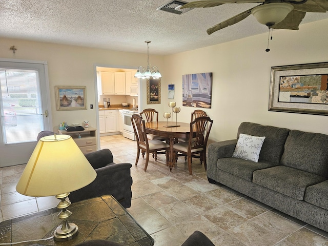 living room featuring ceiling fan with notable chandelier and a textured ceiling