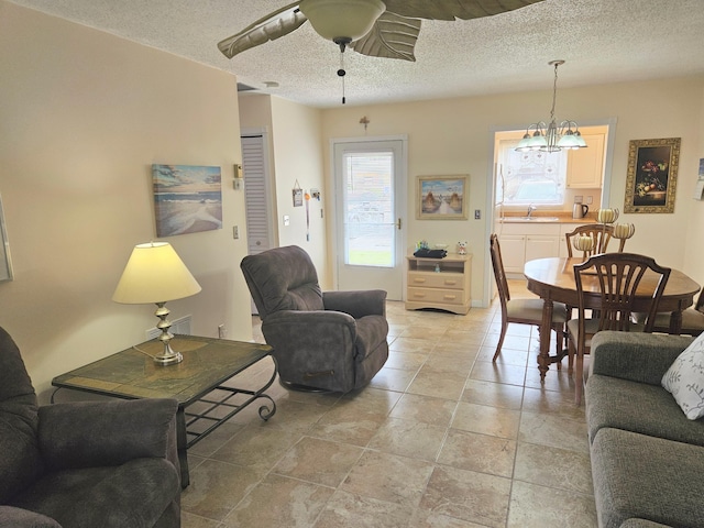 living room with ceiling fan with notable chandelier, sink, and a textured ceiling