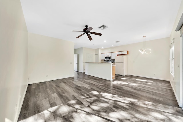 unfurnished living room featuring ceiling fan with notable chandelier and dark hardwood / wood-style floors