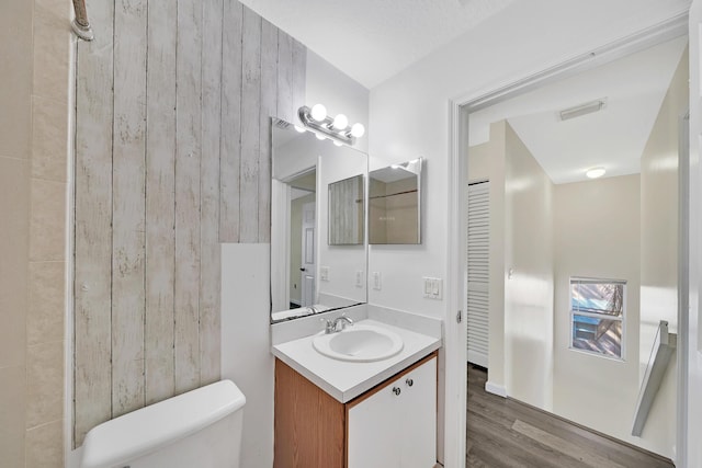 bathroom featuring hardwood / wood-style floors, vanity, toilet, and wood walls