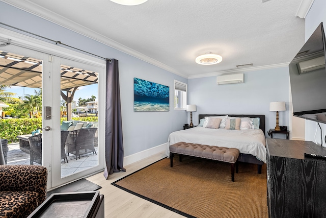 bedroom featuring a wall unit AC, light hardwood / wood-style floors, a textured ceiling, access to outside, and ornamental molding