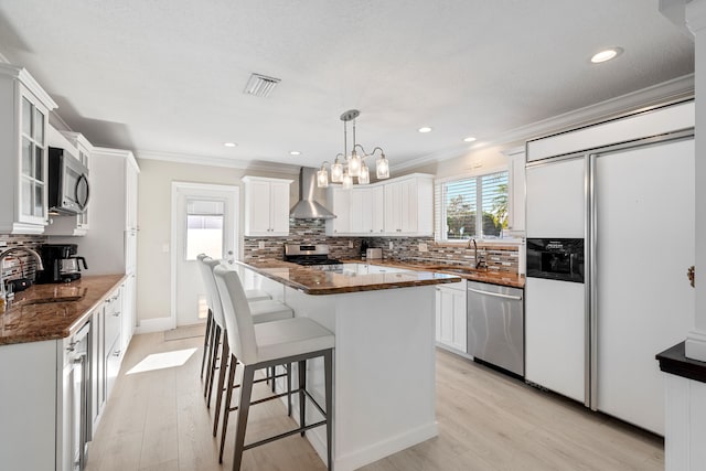 kitchen with wall chimney exhaust hood, white cabinetry, stainless steel appliances, and dark stone counters