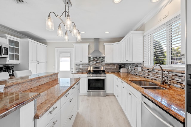 kitchen featuring appliances with stainless steel finishes, sink, wall chimney range hood, white cabinets, and hanging light fixtures