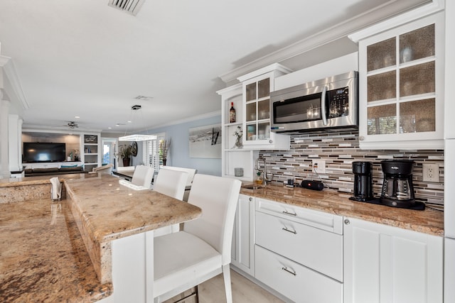 kitchen with backsplash, white cabinets, light stone countertops, ornamental molding, and a kitchen bar