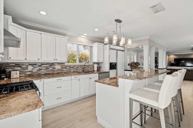 kitchen with light stone countertops, a center island, sink, hanging light fixtures, and white cabinets