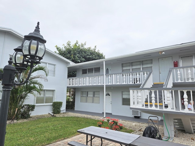 rear view of house featuring an AC wall unit, a yard, and a balcony