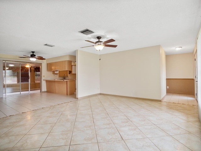 unfurnished living room with ceiling fan, sink, light tile patterned floors, and a textured ceiling