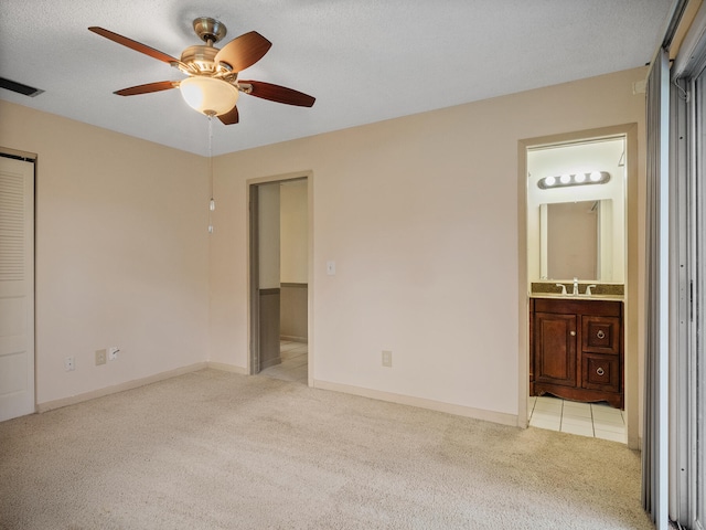 unfurnished bedroom with a textured ceiling, light colored carpet, ensuite bath, and ceiling fan