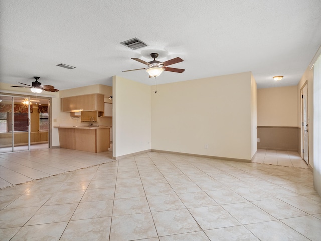 unfurnished living room with ceiling fan, light tile patterned flooring, and a textured ceiling