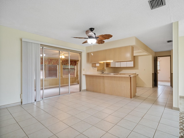 kitchen featuring ceiling fan, kitchen peninsula, a textured ceiling, light brown cabinetry, and light tile patterned floors