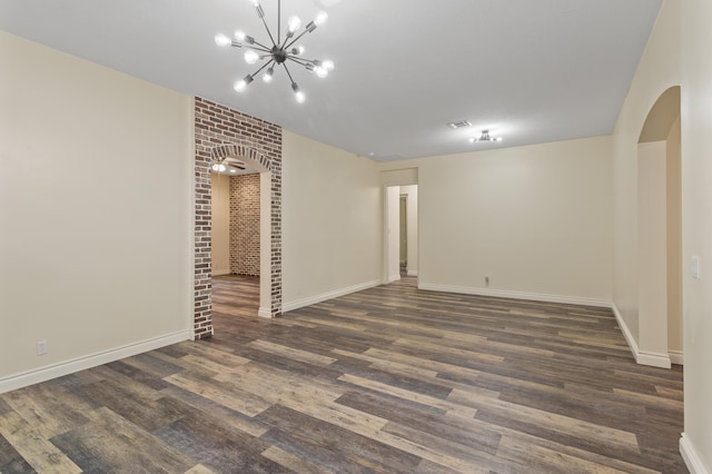 spare room featuring a notable chandelier, dark hardwood / wood-style floors, and brick wall