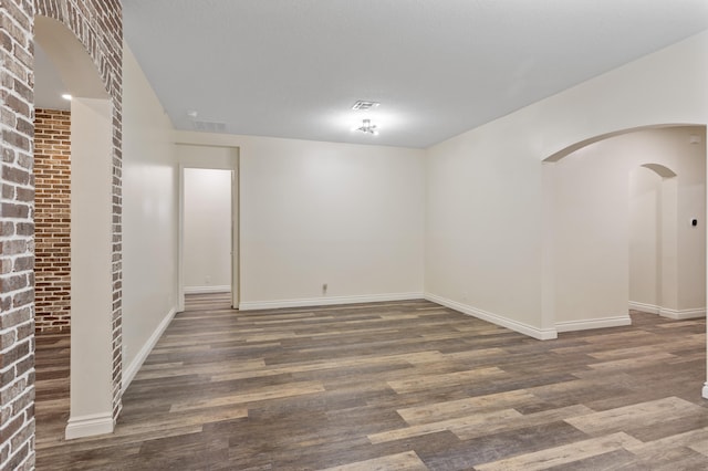 spare room featuring dark wood-type flooring and brick wall