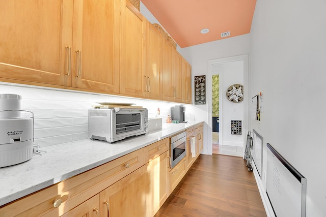 kitchen with stainless steel microwave, light brown cabinetry, light stone counters, and hardwood / wood-style floors