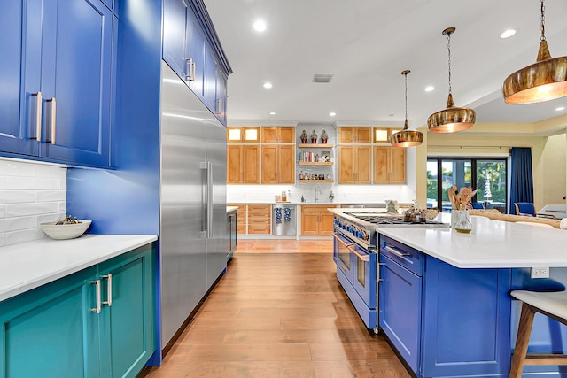 kitchen featuring high quality appliances, blue cabinets, decorative backsplash, light wood-type flooring, and decorative light fixtures