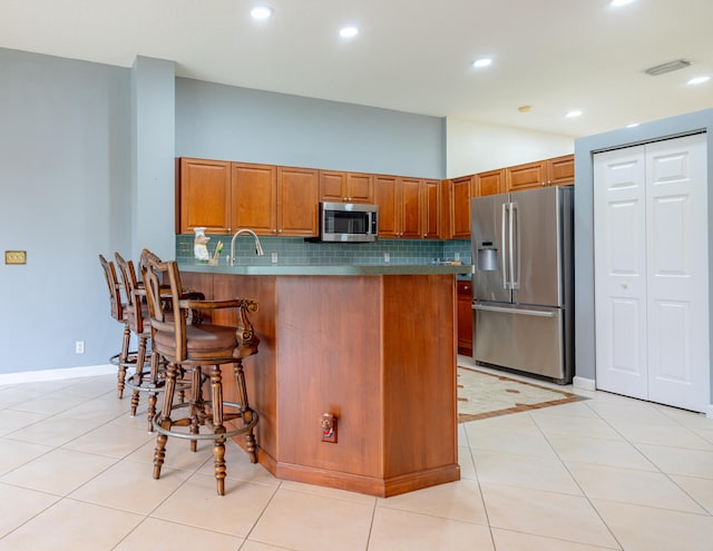 kitchen with backsplash, kitchen peninsula, a kitchen bar, light tile patterned floors, and appliances with stainless steel finishes