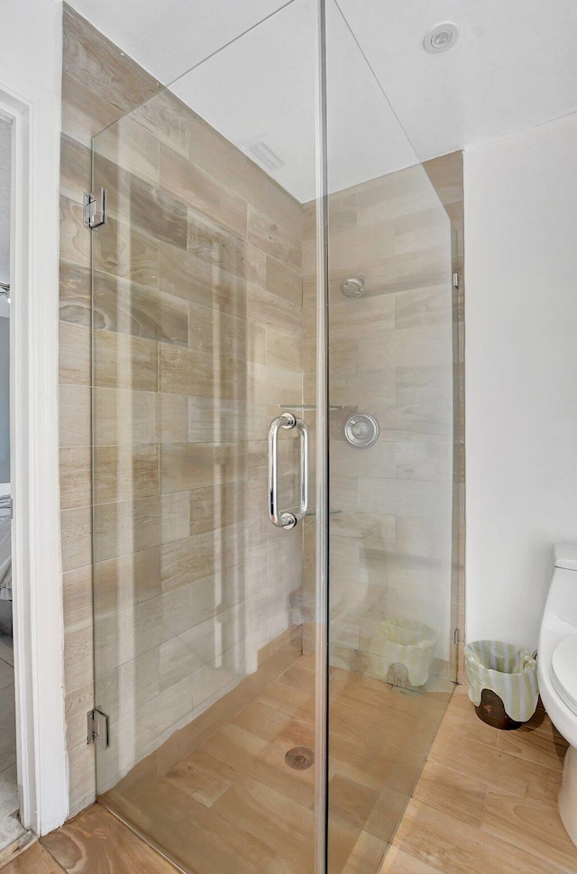 bathroom with wood-type flooring, an enclosed shower, and toilet