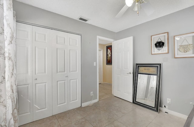 unfurnished bedroom featuring light tile patterned floors, a textured ceiling, a closet, and ceiling fan