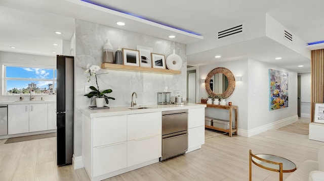 bar with white cabinets, decorative backsplash, light hardwood / wood-style floors, and sink